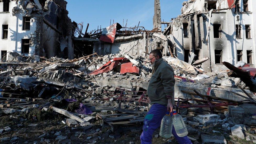 A man carries bottles of water as he walks past the building of a destroyed theatre in Mariupol