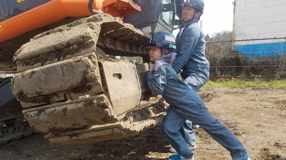 Masato Nakajima and daughter pretend to lift a digger