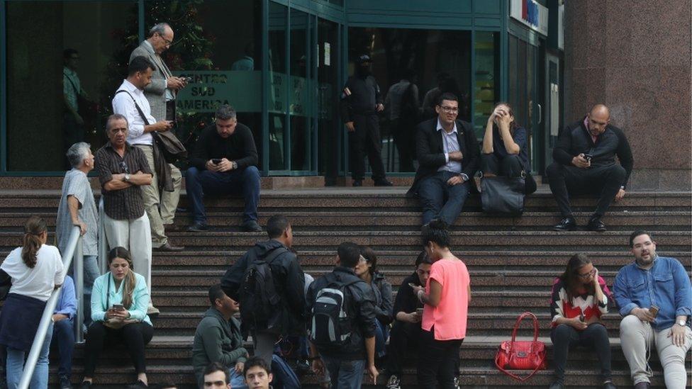 People wait outside of the building with the office of Venezuela's Opposition leader Juan Guaido, in Caracas. 21 Jan 2010