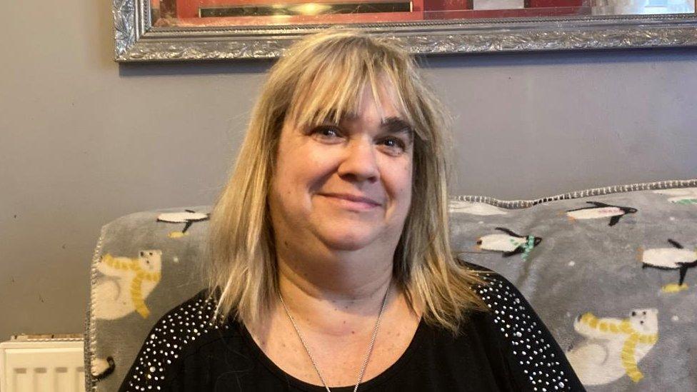 Woman with long blond hair wearing a black top and sitting on a sofa