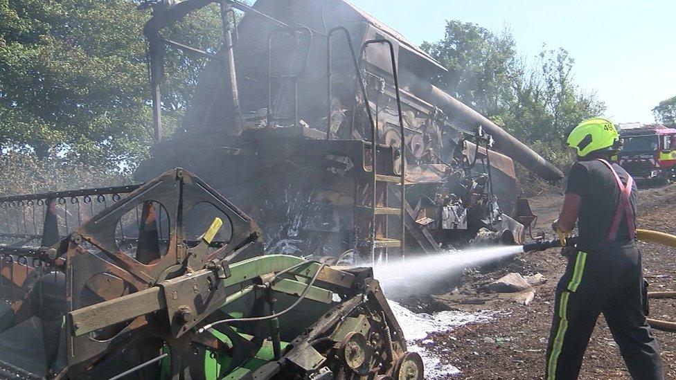 Burnt farm machinery and firefighter with hose