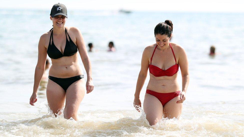 Two women walk up a beach after swimming in the sea