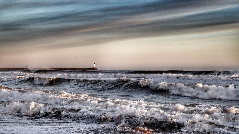 Breaking waves in front of a lighthouse with dark clouds above