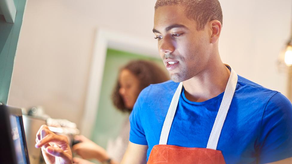 A young coffee-shop worker entering an order into a digital display screen