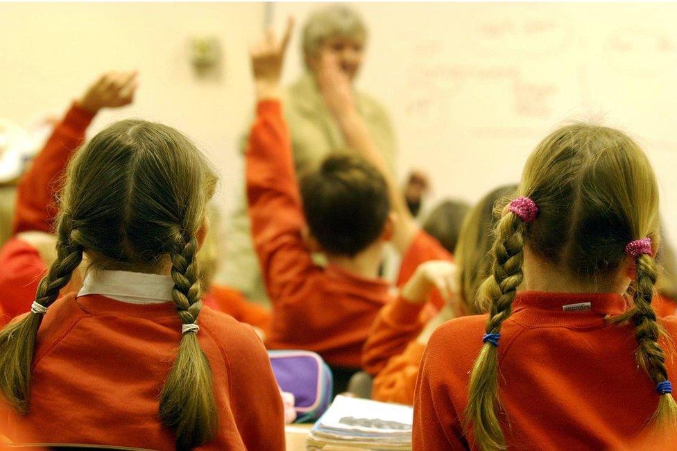 Children in a classroom, some with hands up