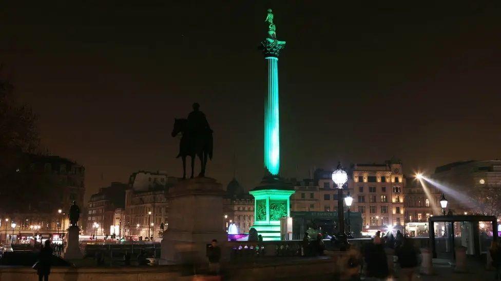 Nelson's Column in Trafalgar Square, London lit in green.