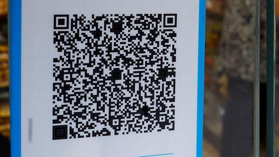 Black and white QR code on a blue-bordered white poster stuck on the window of a shop