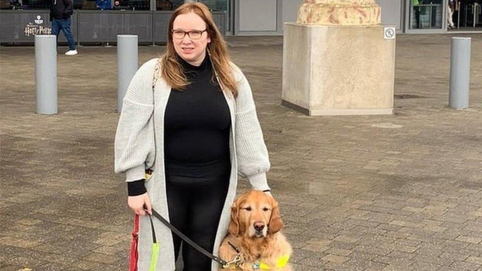 Angharad Paget-Jones with her dog Tudor. She is standing outside a busy shopping centre