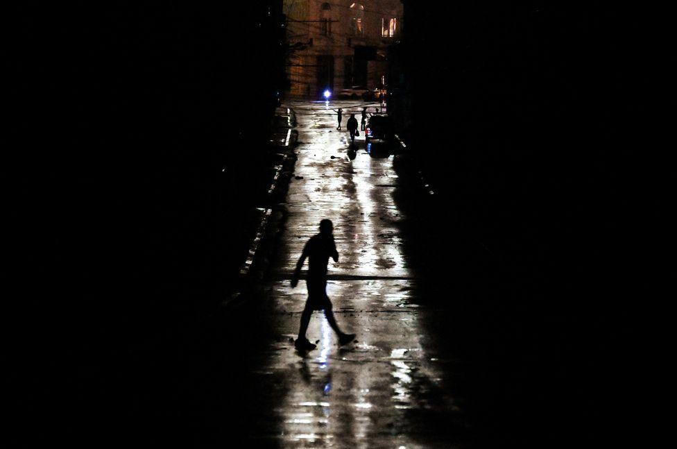 People walk on a darkened street due to a blackout following hurricane Rafael in Havana