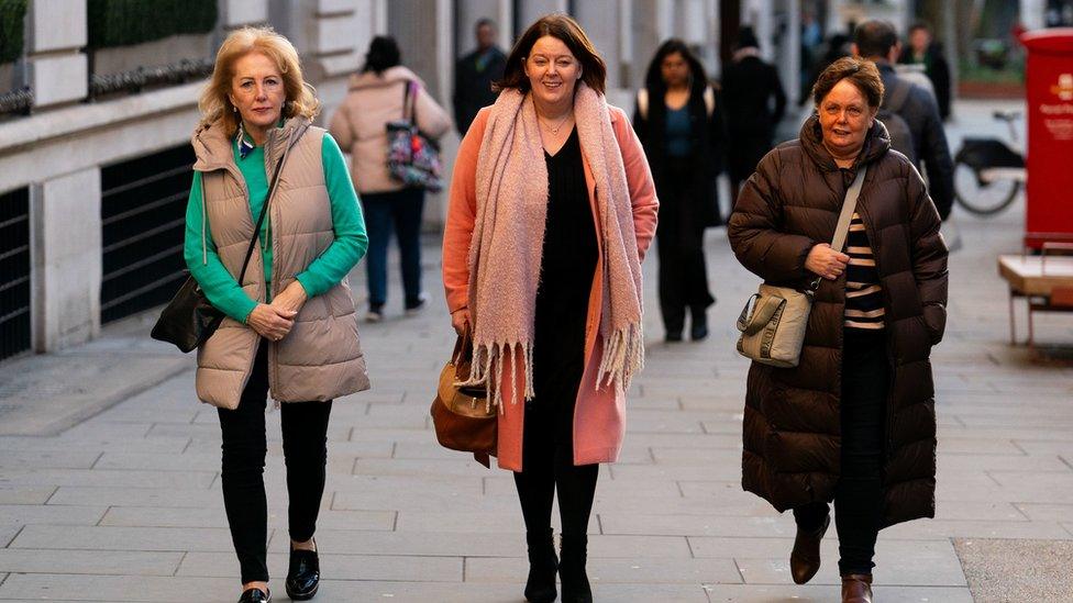 three women in winter coats walking through a London street