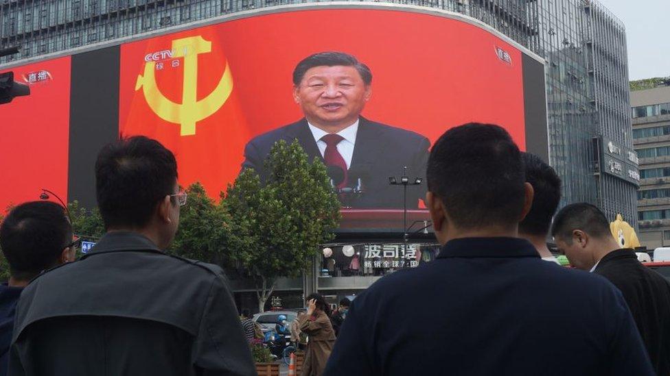 Pedestrians stop at a crossing where a giant screen televising a speech by Xi Jinping at closing ceremony of the 20th National Congress of the Communist Party of China in Hangzhou.