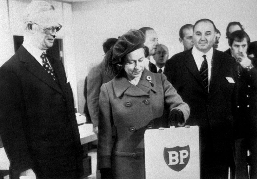 Industry - The Queen Inaugurates the Production of North Sea Oil from Forties Field to BP's Grangemouth - Aberdeen. The Queen, flanked by Sir Eric Drake and Mr Colin Smith, presses a button in the control room at Dyce, near Aberdeen, to launch the flow of oil from the Forties Field in the North Sea to BP's Grangemouth refinery 237 miles away