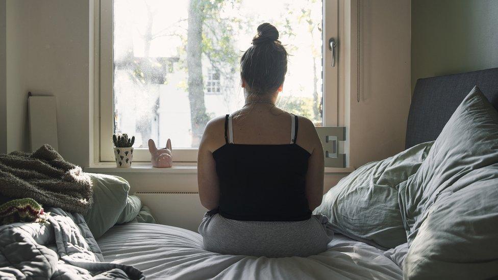 Teenage girl looking out of the window whilst sitting on her bed