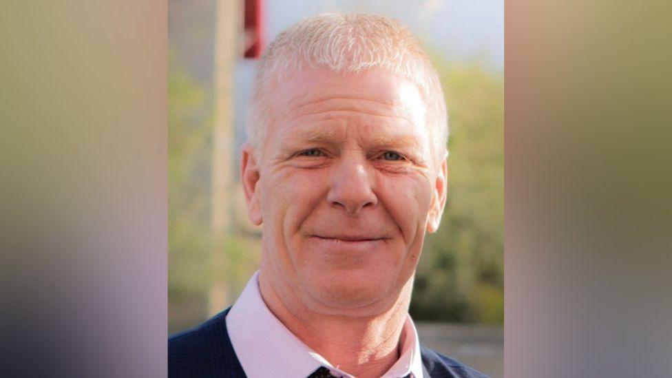 A Facebook picture of Colin Scott looking straight at the camera. He has short, white hair and is smiling