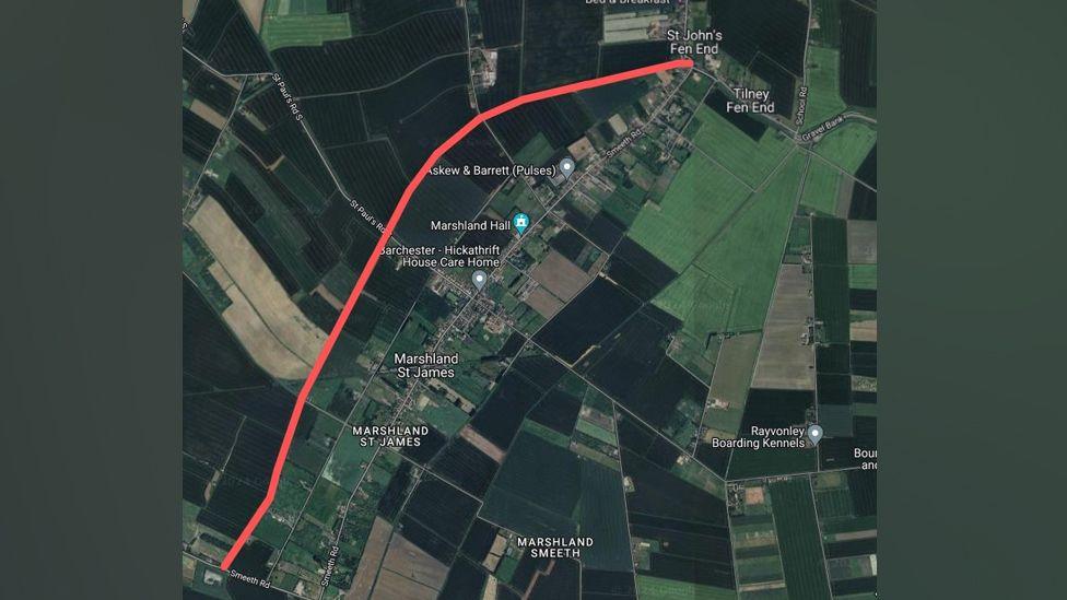 An aerial satellite style map showing the footpath highlighted in red, stretching from the top of the map at St John's Fen End down to Smeeth Road. The fields are dark and light green.