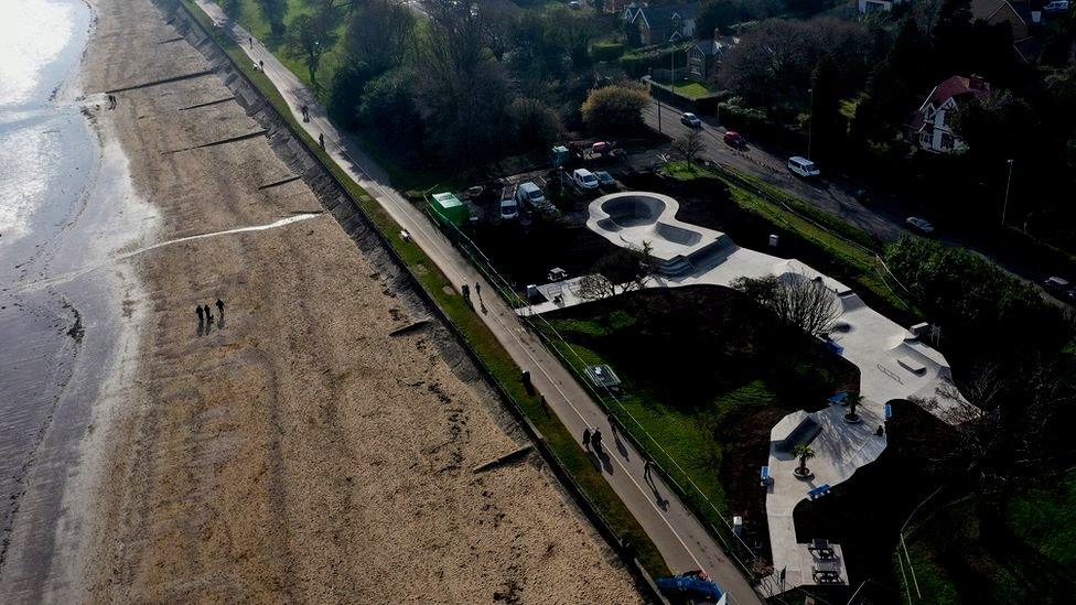 Aerial view of the skatepark, which is a light coloured concrete snaking through grass and trees beside the coastal path and beach