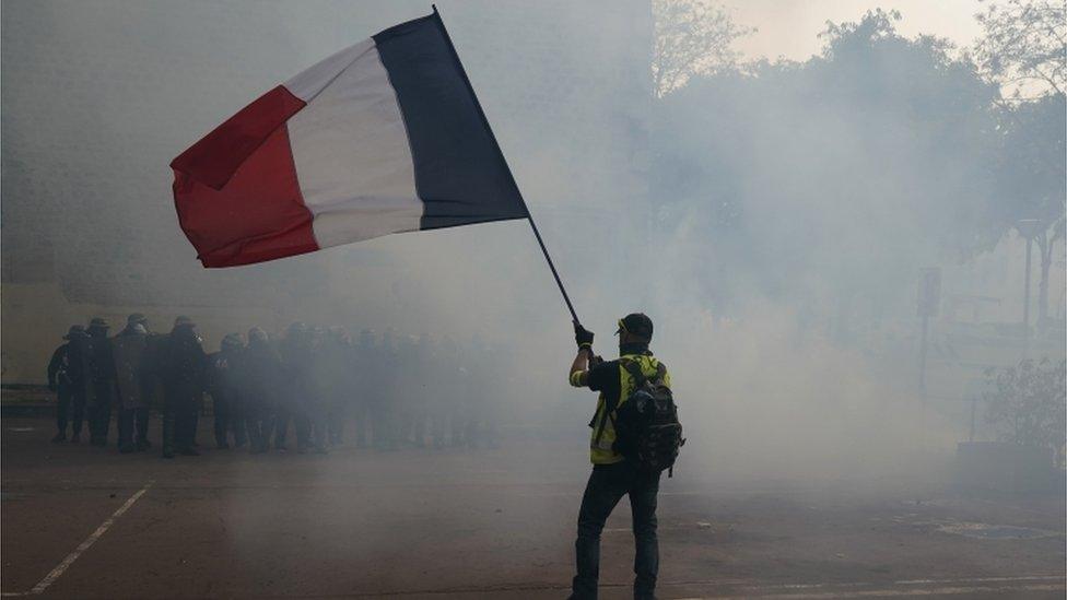 A protester holding a French flag in front of riot police in Paris