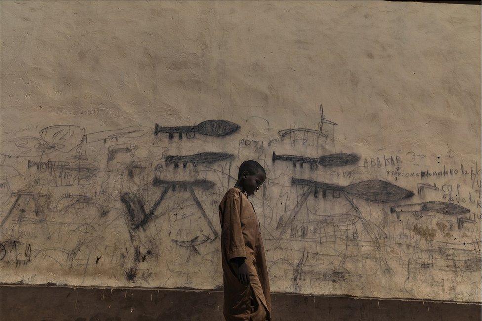 A child stands in front of wall covered in drawings