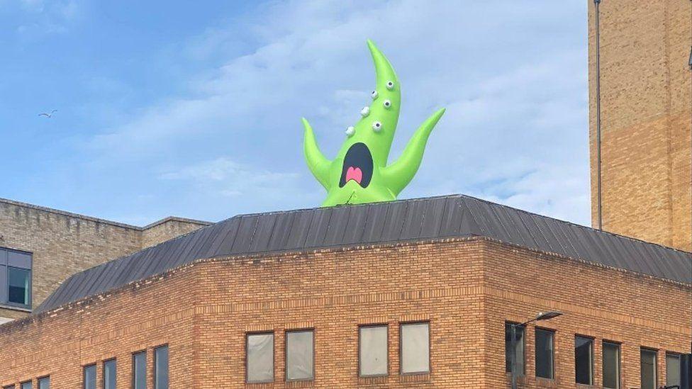 Flame-shamed bright green monster with mouth open and multiple eyes