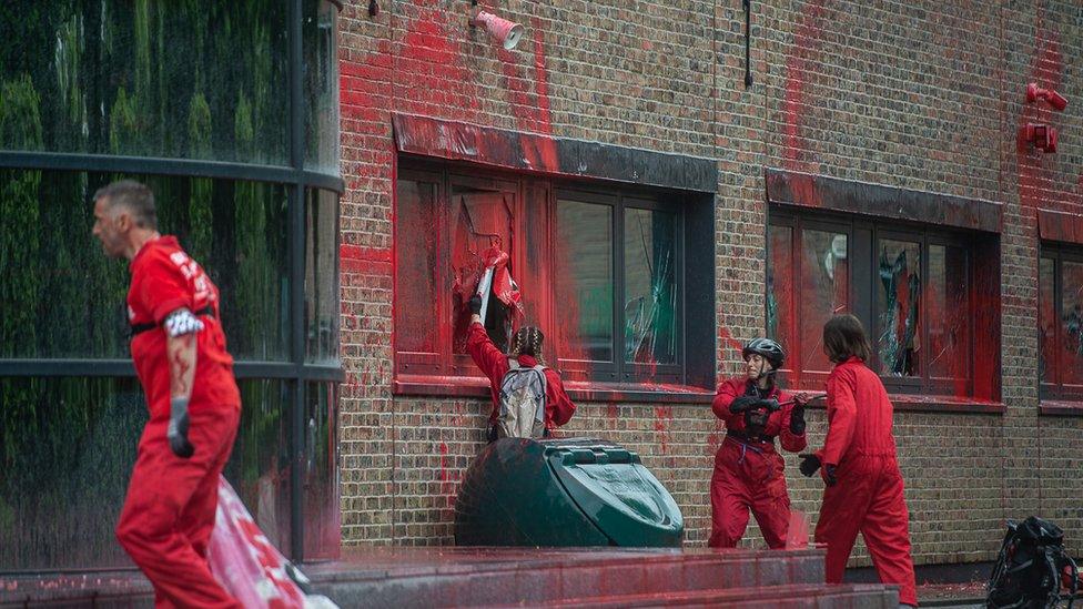 Members of the Palestine Action protest group dressed in red overalls, throwing red paint over the Elbit building and smashing windows