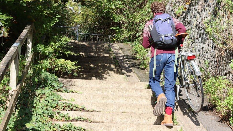 A person with a backpack on carrying a bike up stairs outside