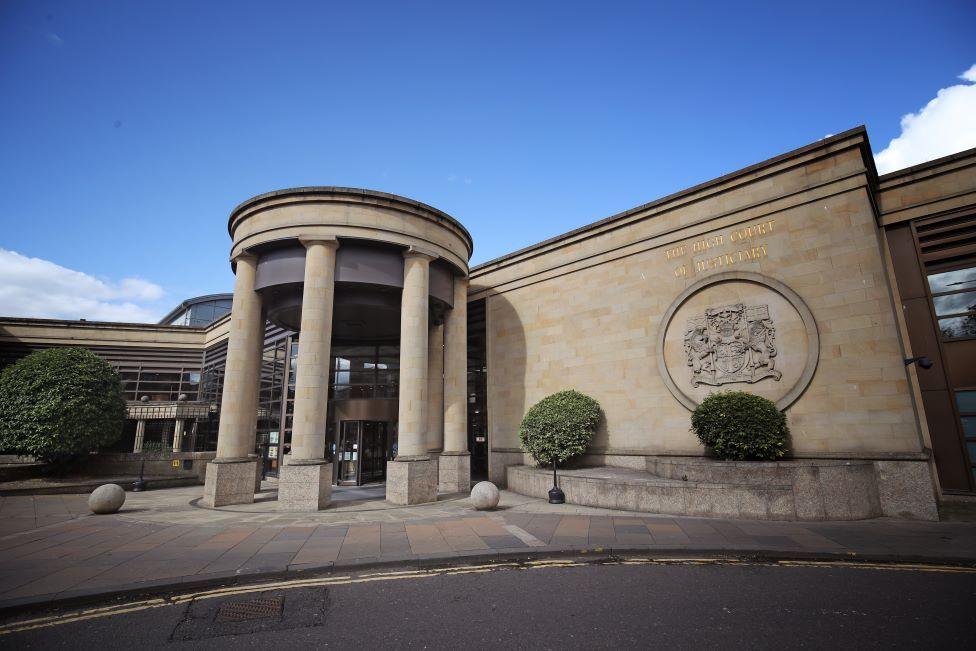 The High Court in Glasgow is a sandstone building with a grand entrance through a circle of tall columns. The city's crest is emblazoned on the wall by the entrance.