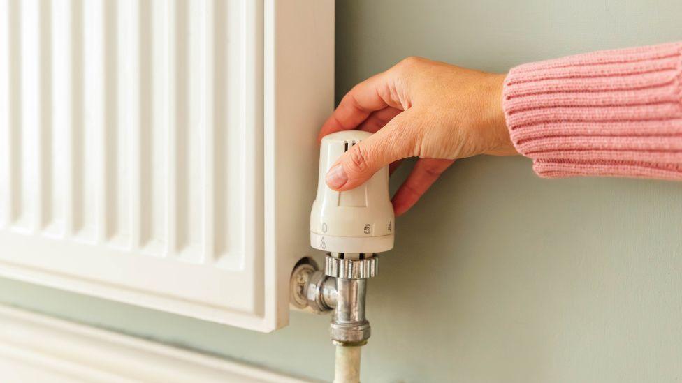 A woman's hand adjusts the thermostat on a radiator 