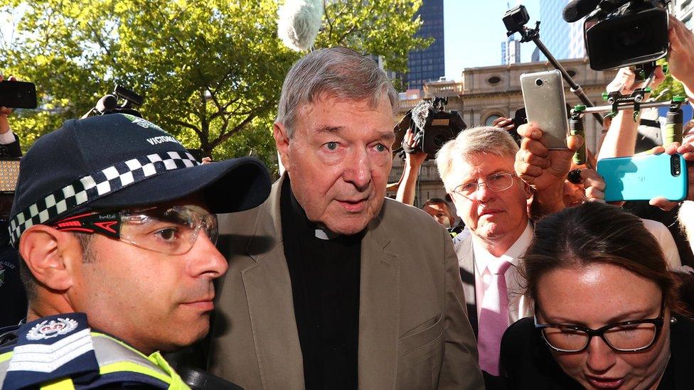 George Pell is escorted by police through a crowd of media and onlookers outside a Melbourne court at the start of his sentence hearing.