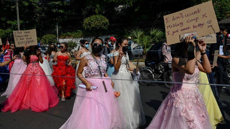 Myanmar women in ball gowns holds up placards during a demonstration against the February 1 military coup in Yangon on February 10, 2021