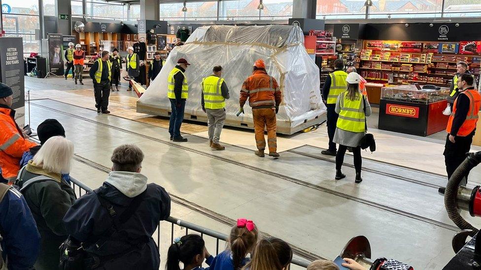 People watch as the wrapped up Locomotive is pushed into the museum building on trolleys