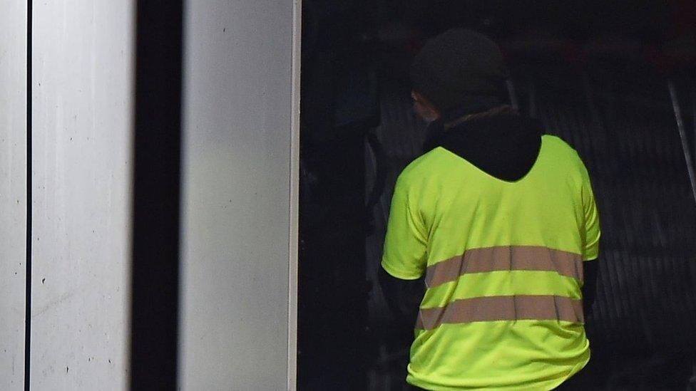 A man wearing a yellow vest and reportedly wielding a grenade, which could be a tear gas, stands as police carry out an intervention at the car wash station of the Espace Anjou shopping centre in Angers, western France,