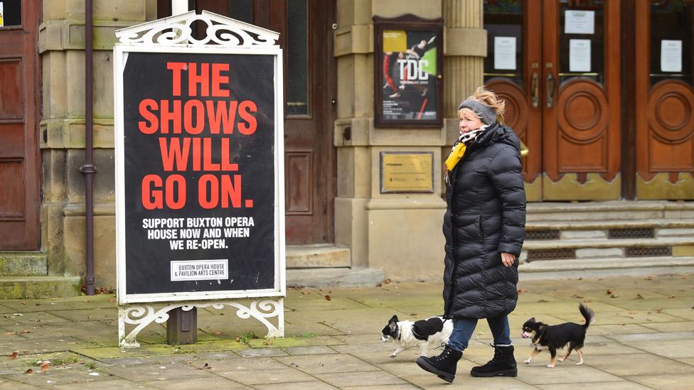 Woman walking past a theatre sign saying "The shows will go on"