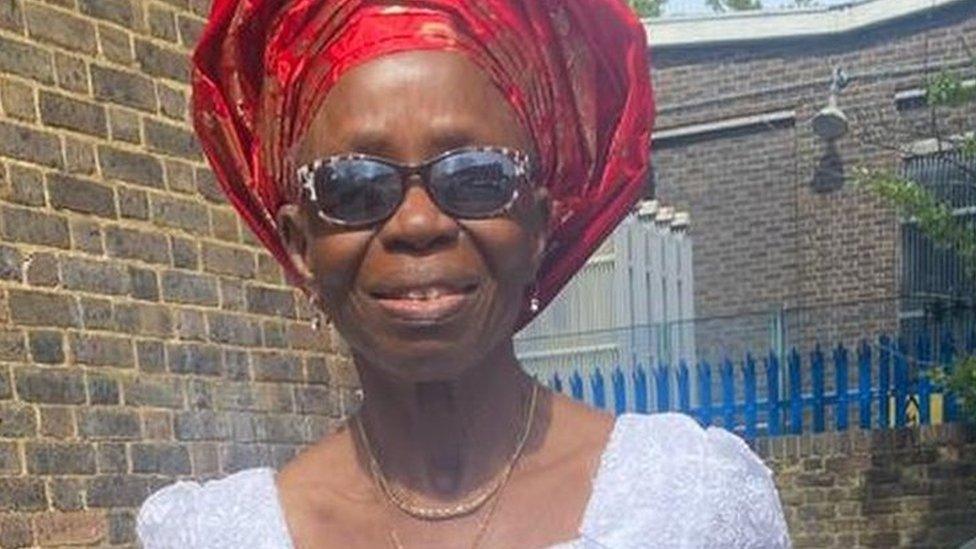 Nelly Akomah, wearing a red headdress, sunglasses and white top.