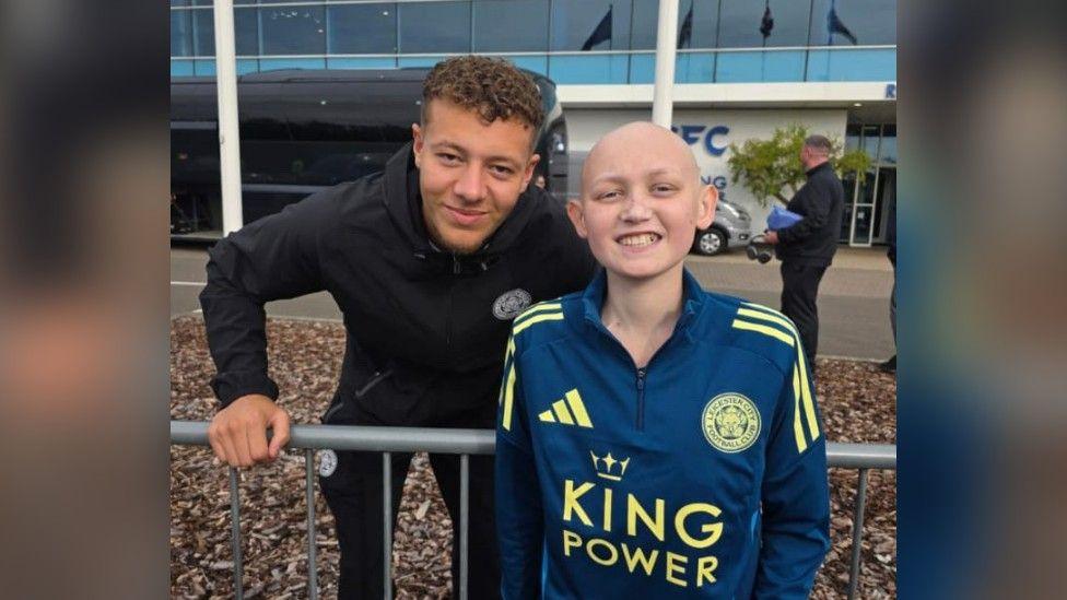 Harrison wearing a Leicester City football kit outside the King Power Stadium meeting his favourite Foxes player Kasey McAteer 