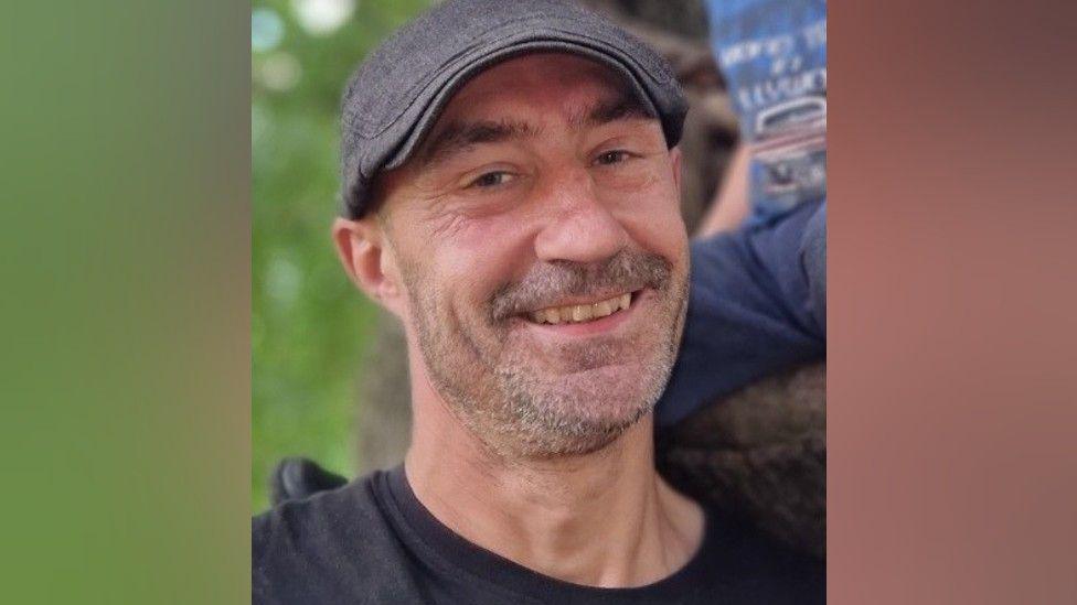 Stefan Watkins, smiling and wearing a grey flat cap and black t-shirt