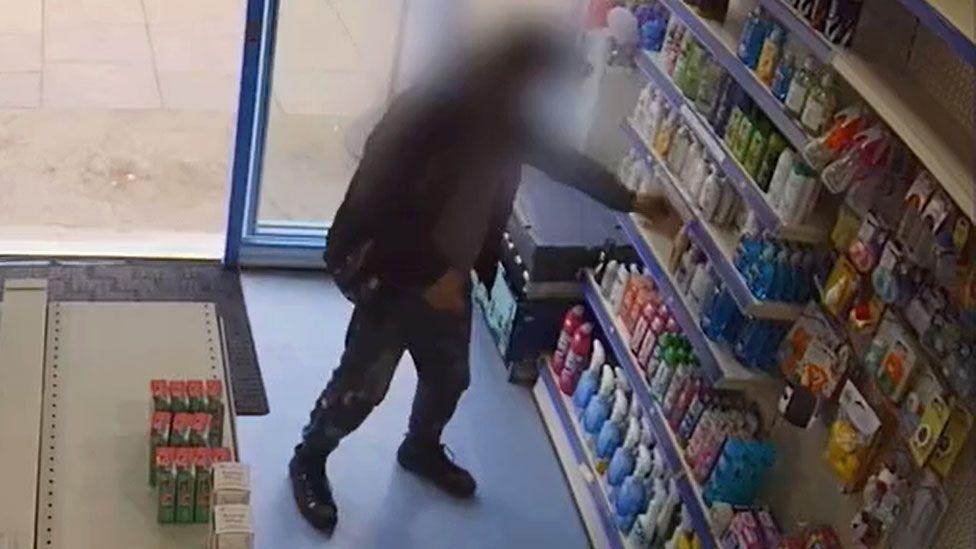 A man with a blurred face takes an item off of a shelf