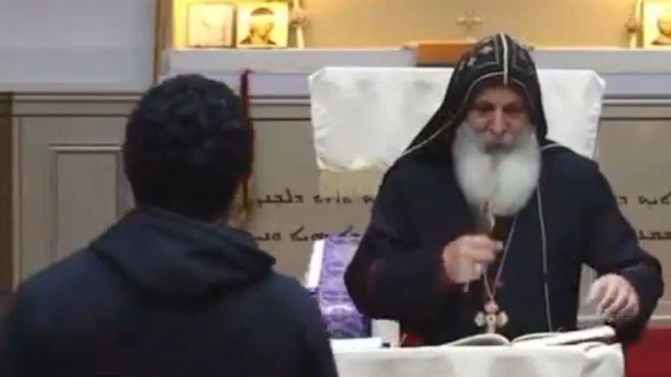 Screenshot of a man walking up to a bishop giving a sermon