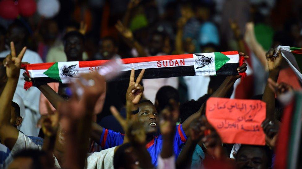 Sudanese protesters wave flags and flash victory signs as they gather for a sit-in outside the military headquarter