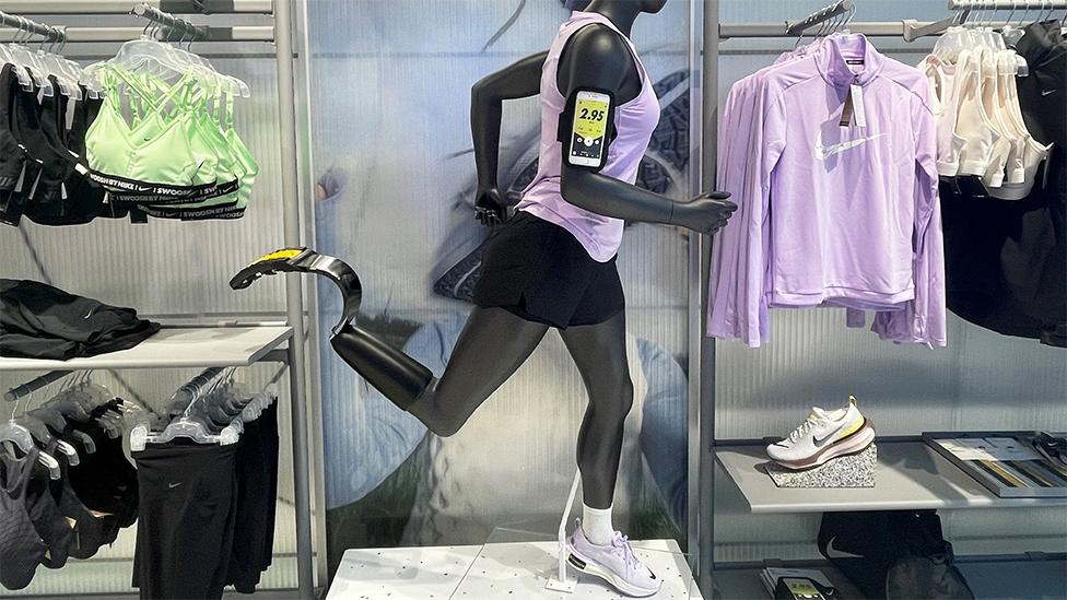 An amputee mannequin in a Nike store with one running shoe and one running blade