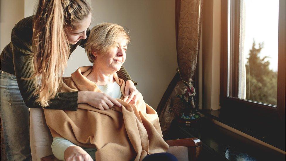 A young girl puts a blanket around a woman