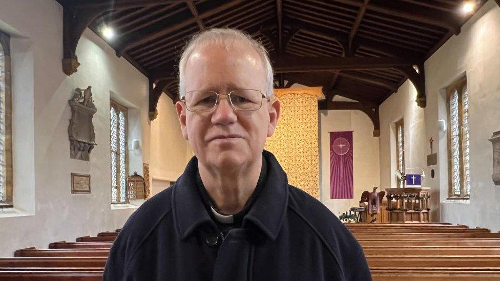 Man with very short hair and glasses wearing a white collar