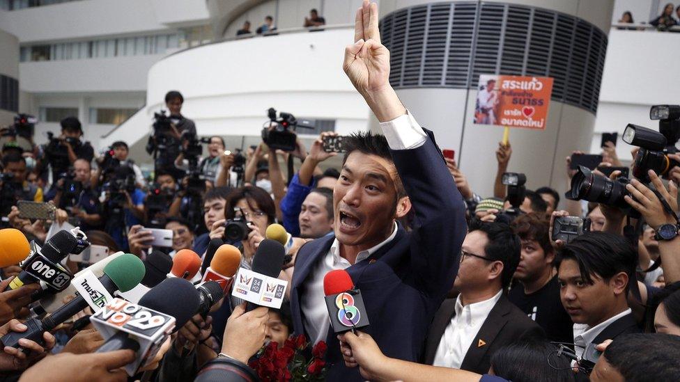 FutThanathorn Juangroongruangkit, dressed in a suit and raising his arm, is surrounded by journalists as he arrives at court