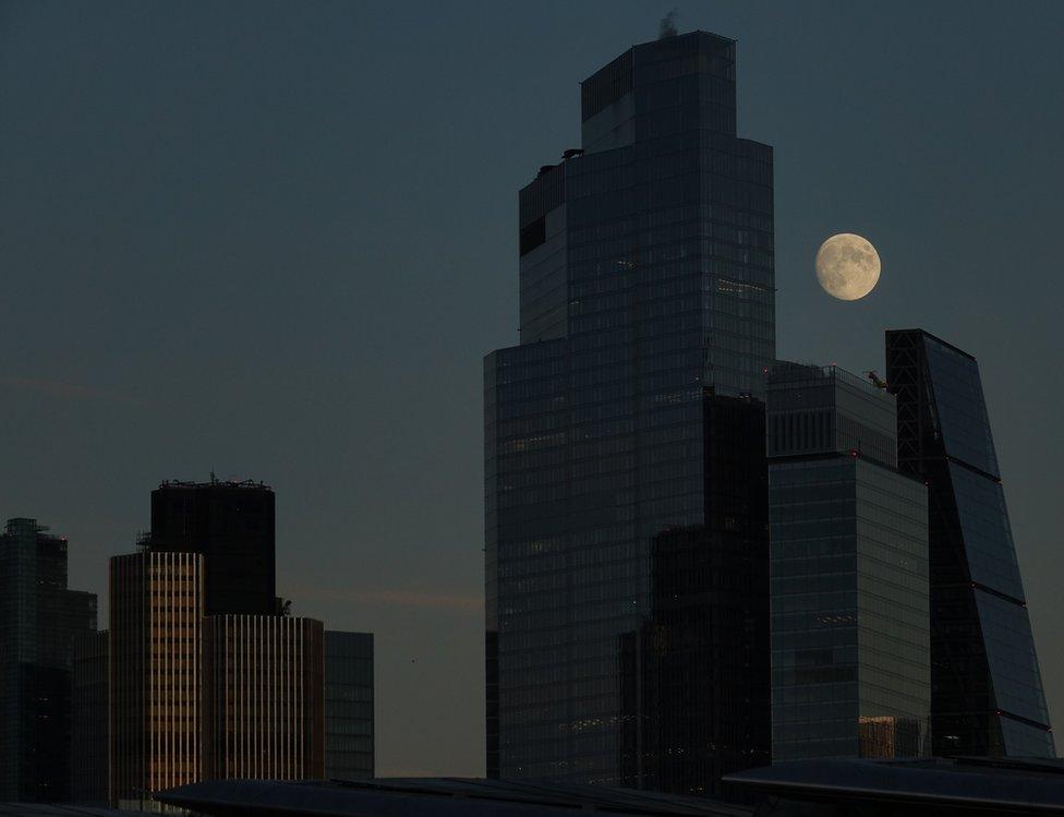 A nearly full-moon behind buildings