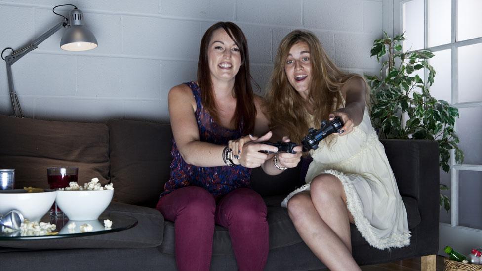 Two young women with cheerful expressions playing video games on a sofa