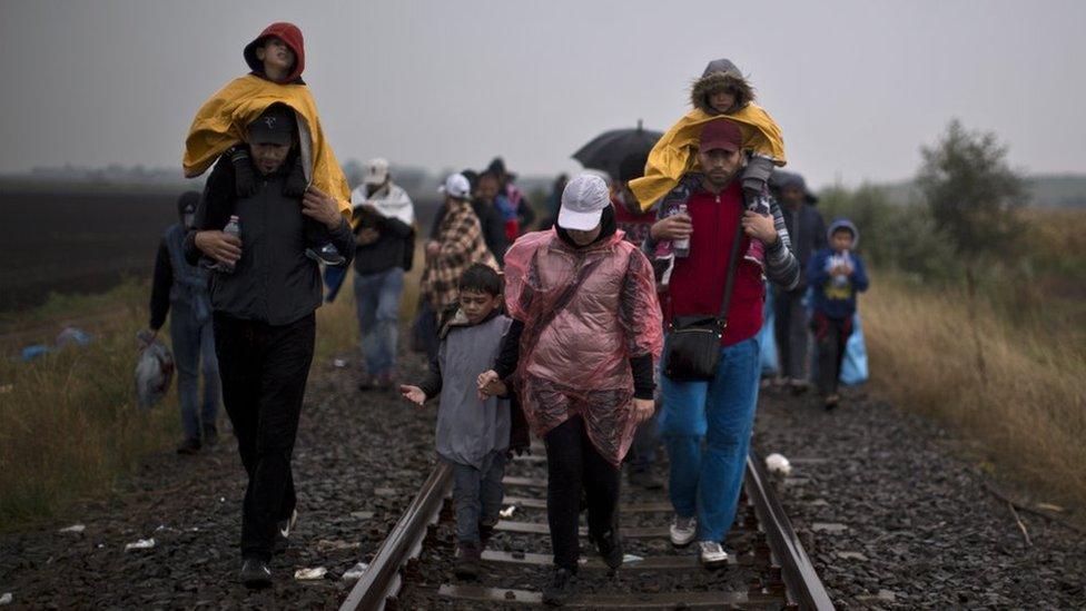 Syrian refugees walk on a railway track