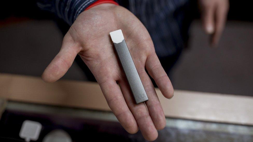 Ryan Purington, an employee at Lucky Juju, holds a JUUL vape in his hand.