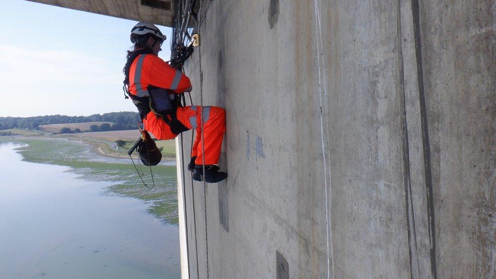 Worker is suspended under the carriageway of the bridge, above the ground.