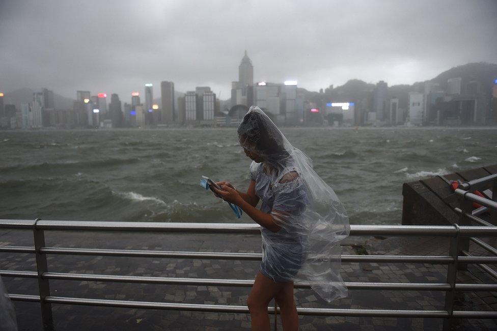 A woman uses her phone while wearing a plastic poncho along Victoria Harbour during heavy winds and rain brought on by Typhoon Hato in Hong Kong on 23 August 2017.