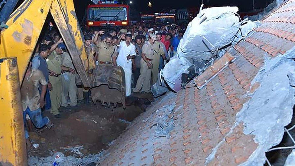 Indian officials and bystanders gather beside a collapsed building after an explosion and fire at The Puttingal Devi Temple in Paravur