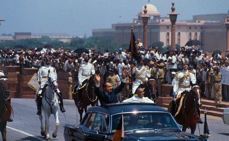 President Richard Nixon waves to crowds as he rides in open car with the acting president of India, Mohammad Hidyatullah, in motorcade from airport upon arrival here July 31.